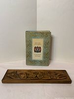 Rectangular wood carved art panel alongside the book titled 'British Columbia: A Centennial Anthology'.