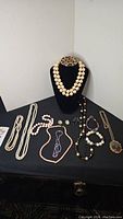 Full assortment of jewelry displayed on a black surface and black bust, includes multiple necklaces, bracelets, earrings, and brooches.