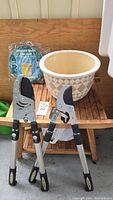 Full lot view showing two loppers, clay planter, and collapsible bucket on wooden table