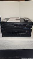 Front view of black Sony CDP-292 disc player stacked on Onkyo TX-8020 receiver with remote control and paperwork on top.
