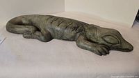 Stone lizard sculpture viewed from side showing elongated body and curled tail details.