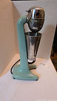 Side view of the teal-colored vintage milkshake maker with metal cup in place.