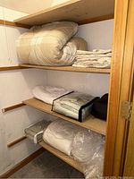 Closet shelf displaying a twin comforter with pillow sham on top shelf, folded bed sheets, Berkshire blanket and mattress protector sheet underneath, all folded neatly.
