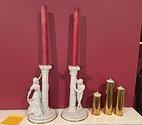 Front view of ceramic Romeo and Juliet candle holders with red taper candles and three brass candle holders with LED candles