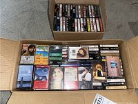 Box of cassette tapes showing a variety of music tapes including some with visible front covers like rock and pop albums.