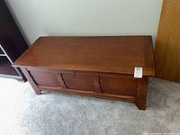 Image of the cedar chest showing front panel with carved detail, medium brown finish, scratches, and scuffs.