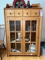 Front view of Canadel wood china cabinet showing double glass paneled doors, four dovetailed drawers, items inside and top shelf with decorative plates and figurine.
