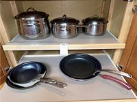 Top shelf: three stainless steel pots with lids; bottom shelf: nested black nonstick pans and purple Klok pan