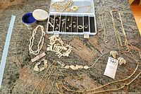 Full view of assorted costume jewelry including necklaces, men's tie clips, cuff links, earrings, and rings laid out on granite counter.