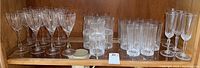 Overall view of all 32 crystal glasses on shelf showing wine, highball, water, and champagne flutes grouped together.