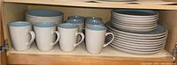 Stoneware mugs, bowls, salad plates, and dinner plates neatly stacked in cabinet
