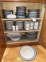 Cabinet view showing full stacks of plates, bowls, mugs, saucers, butter dish, salt and pepper shakers, casserole and platters