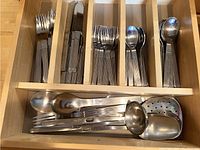 Drawer containing organized flatware including forks, knives, spoons in ribbed handle design and stainless steel cooking utensils