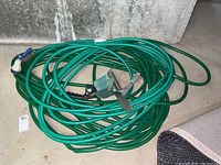 Two coiled green garden hoses with metal wall mount for storage, shown on concrete floor.