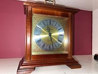 Full view of wooden mantle clock with glass covered brass dial, showing overall design and shape.