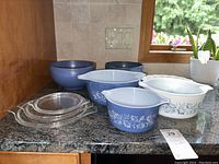 Front view of three blue Pyrex nesting bowls with white floral patterns and matching clear lids, Dansk and pie dish behind.