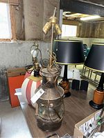 Front angle view of antique railroad lantern on table showing metal body, glass lenses, electric lamp sockets on top with wiring and pull chains.
