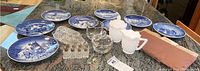 Wide shot showing 8 blue and white Royal Copenhagen plates arranged in a circle, hobnail milk glass creamer and sugar, crystal salt and pepper shakers, crystal sugar and creamer, and the slate cheese board on a granite countertop.
