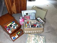 Full lot showing Singer sewing machine, original beige case, wooden box with colorful spools of thread, and wicker basket with sewing notions