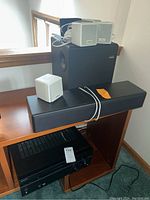 Overall view of the speaker components arranged on furniture showing the large black subwoofer, black soundbar, and small gray satellite speakers