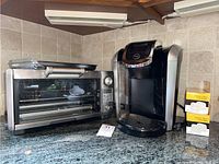 Breville toaster oven with stainless steel exterior, Keurig coffee maker, and two boxes of water filter cartridges on kitchen counter.