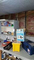 Wide view of basement workbench with tool chests, sump pump box, assorted tools and storage units.