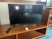 Front view of the Vizio 32-inch LED TV on a wooden shelf with the remote control placed next to it.