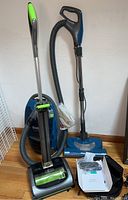 Full view of Kenmore progressive vacuum cleaner with hose, attachments, and Bissell vacuum cleaner in background.