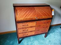 Front view of roll top desk showing curved roll top with key, three drawers with handles, and wood inlay pattern.