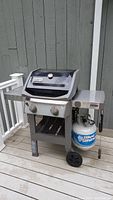 Front view of Weber GS4 gas grill showing control knobs, lid, and propane tank below.