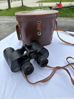 Photo showing vintage binoculars with leather case outdoors on a white cloth