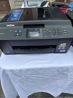 Front view of Brother MFC-J430w printer showing control panel, LCD screen, and inkjet output area on white cloth background.