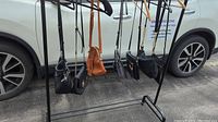 Seven crossbody bags hanging on rack in various colors including black and brown, showing different lengths and strap styles.