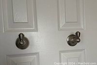 Two brushed nickel door hooks mounted on a white door, showing their size and placement.