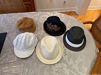 Top-down view of five assorted hats on a patterned tablecloth, showing various styles and colors.