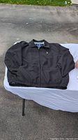 Full view of black men's Polo jacket laid flat on a surface showing front, long sleeves, collar and elastic waistband.