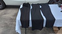 Three pairs of women's black dress pants laid side by side on a table outside, showing full length and overall style.
