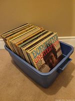 Bin full of vinyl records showing The Doobie Brothers Greatest Hits album cover on front, albums stacked vertically in blue plastic bin.