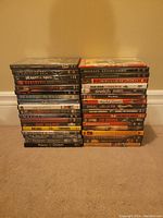 Photo showing 36 DVDs stacked in two columns on carpeted floor against wall, various movie titles visible on spines.