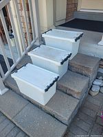 Three white vintage Canada Post storage bins with black locking lids, placed outdoors on stairs.