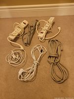Photo showing three power bars with multiple outlets and three extension cords of different lengths and plug types laid out on carpeted floor.