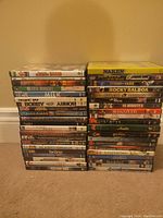 Photo of 41 DVD cases stacked in two piles against a beige wall, showing a variety of movie titles and cover art.