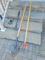 Four garden tools on stone steps: a shovel, a garden rake, a handheld weeder, and a rotary cultivator, all used