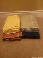 Four folded bath towels stacked in two rows with yellow and gray towels on top, brown and navy blue towels on bottom.