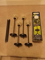 Photo showing five solar powered outdoor garden lights with glass globes and black stakes, along with the original box.