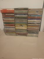 Three stacks of over 80 music CDs, mainly classical and jazz genres, in jewel cases placed on a flat surface against a wall