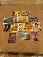Photo showing 14 assorted postcards laid out on a carpeted floor with a variety of scenic, vintage, and cultural images.
