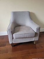 Front angled view of gray upholstered armchair showing cushion, armrests, and wooden legs.