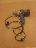 Photo showing a blue and black corded electric impact wrench with metal front and attached power cord with two-prong plug. The tool shows signs of wear and damage.