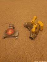 Photo showing two lawn hose attachments placed on a beige carpet: a metal sprinkler attachment with a perforated copper-colored head and a gray plastic dual hose splitter with yellow valves.